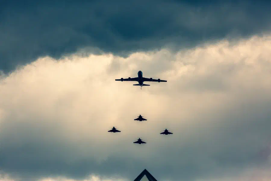 A tanker aircraft leading four fighter jets in formation under storm clouds