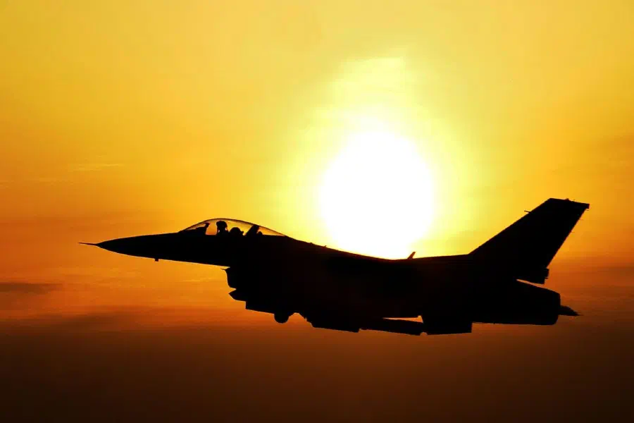 Silhouette of a fighter jet in flight against the setting sun