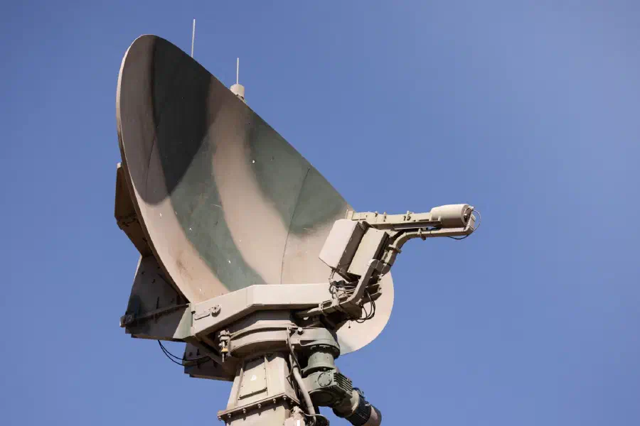 A camouflage-painted military radar dish against a blue sky